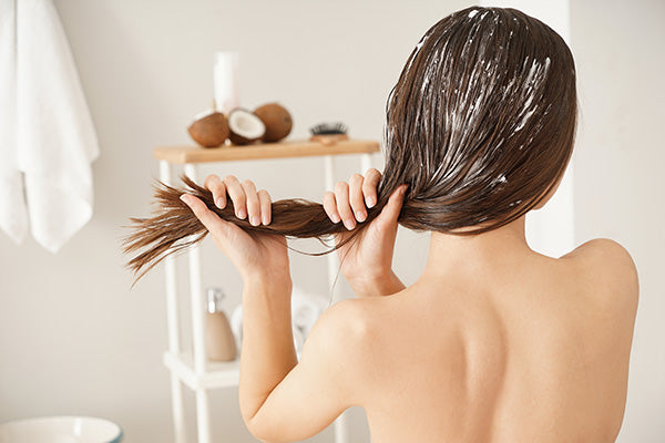 woman applying coconut oil to long hair extensions