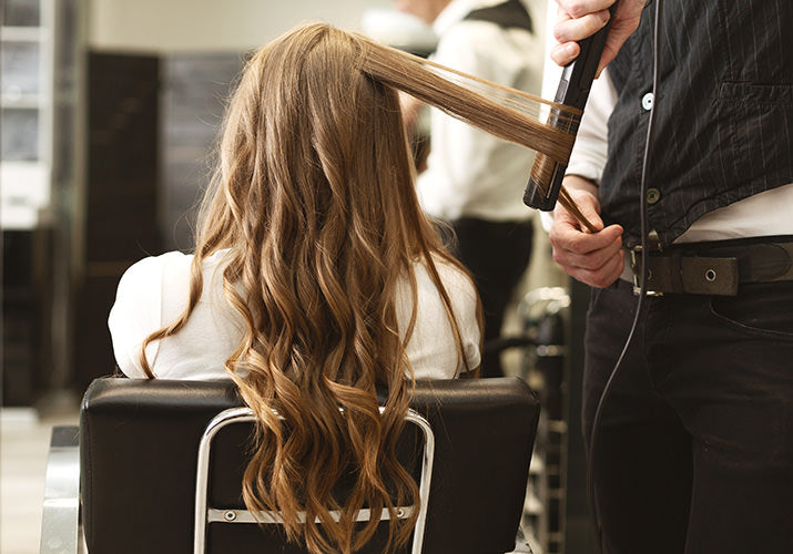 Stylist with client in chair curling long extension hair