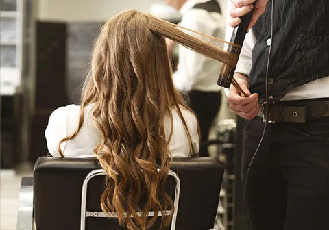 Stylist with client in chair curling long extension hair