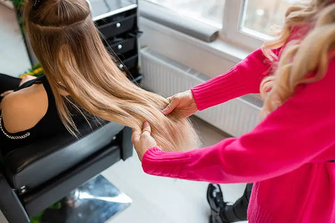 stylist looking at client's hair to see the blend of blonde extensions with the natural hair color