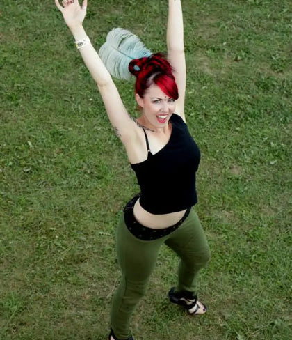 A woman with vibrant red hair styled in a high bun, wearing a black crop top and olive green pants.