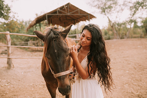 brunette woman with long curled hair extensions with her horse