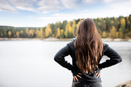 woman with long healthy hair extensions standing in front of a lake