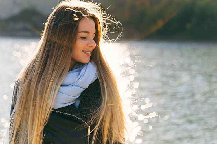 Woman with long hair extensions fading from brunette to blonde in front of a lake