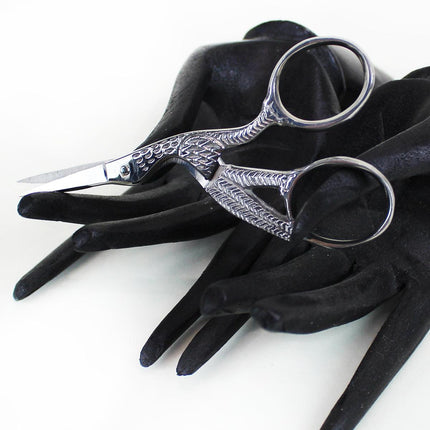 Metal stork scissors in black mannequin hands on white background
