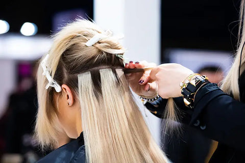 stylist installing a row of tape hair extensions on a client